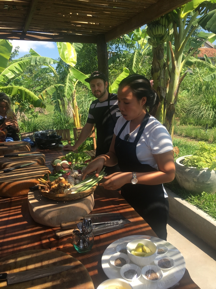 Des personnes participant à un cours de cuisine en plein air avec des ingrédients sur une table.