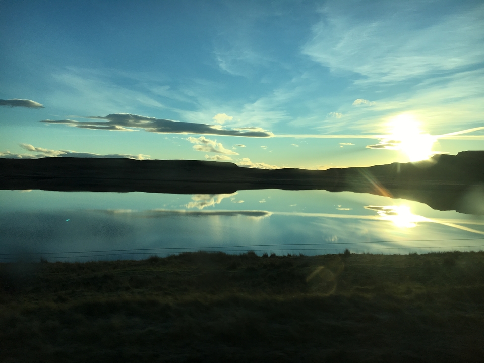 Soleil se couchant au-dessus d'une étendue d'eau calme avec des nuages reflétés à la surface.
