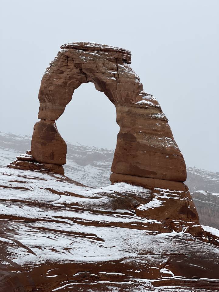 Arche rocheuse naturelle avec de la neige sous un ciel nuageux.