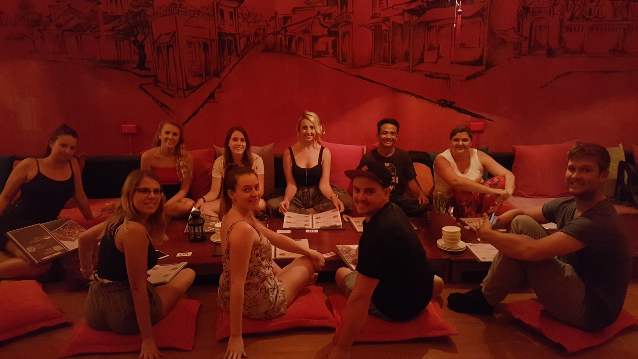 Grand groupe assis autour d'une table basse lors d'un rassemblement faiblement éclairé.