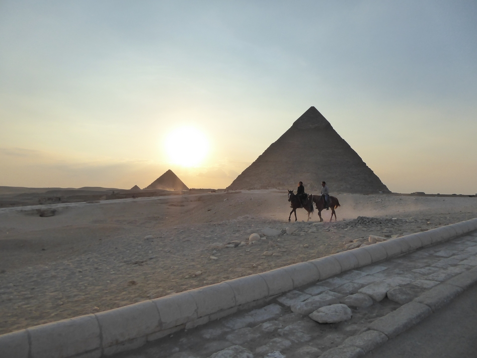 Deux personnes à cheval devant les pyramides au coucher du soleil.