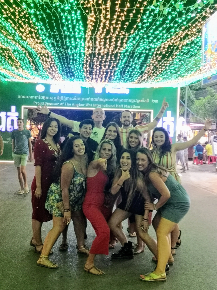 Groupe de personnes posant joyeusement devant un panneau du semi-marathon d'Angkor Wat.