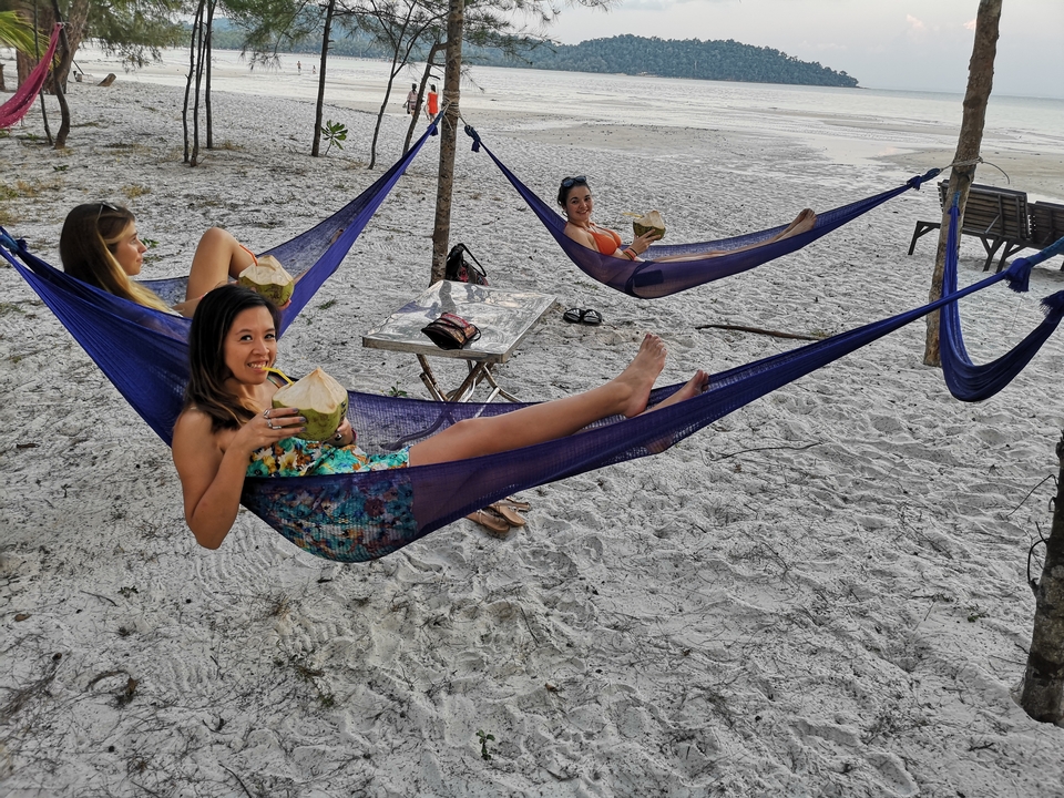 Des gens qui se détendent dans des hamacs sur une plage de sable, buvant de l'eau de coco.