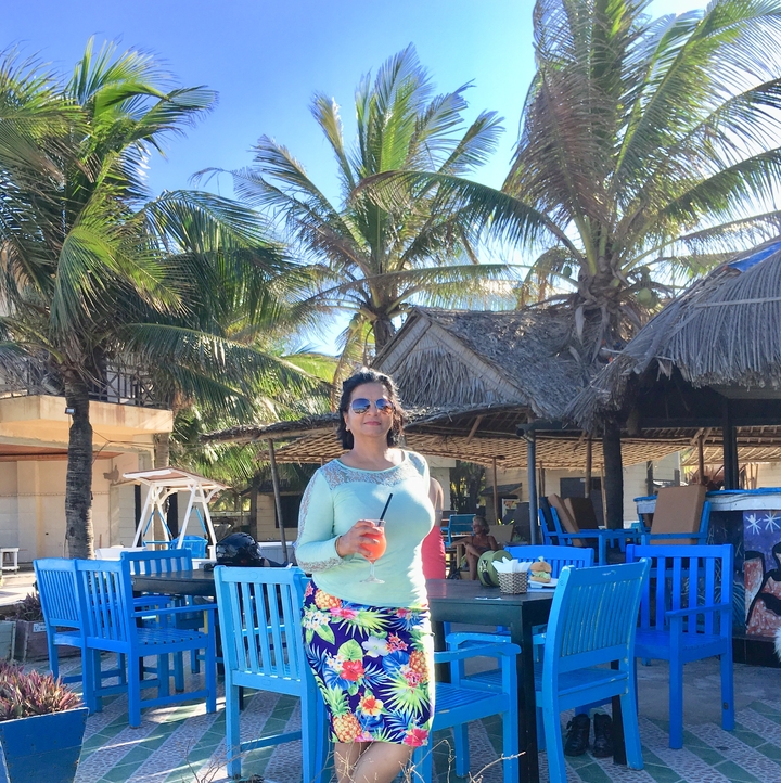 Femme savourant un verre dans un restaurant tropical en bord de mer.