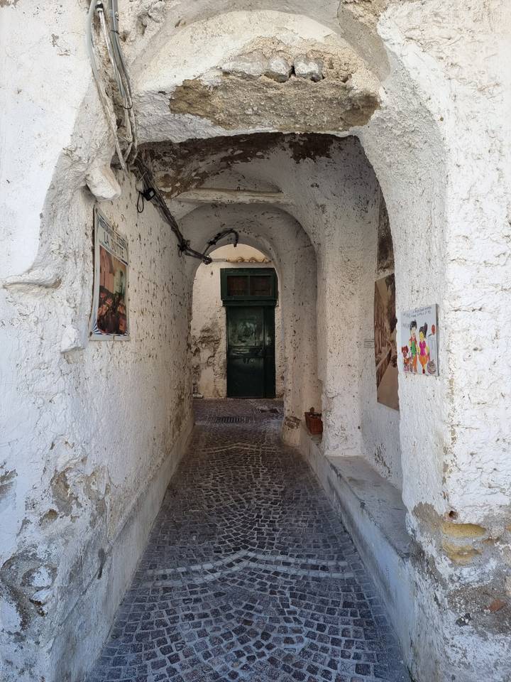 Ruelle étroite pavée de galets avec des murs et portes rustiques blancs.
