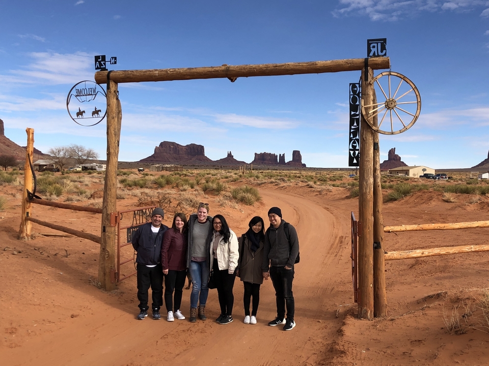 Groupe de personnes posant sous un portail de ranch avec des formations rocheuses en arrière-plan.