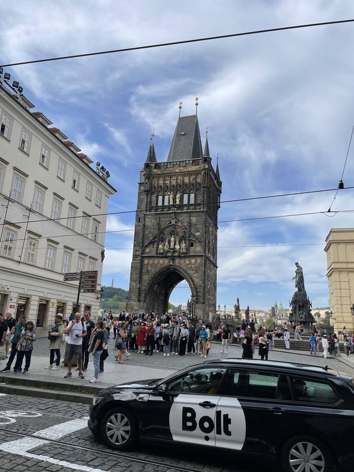 Tour historique avec arche et foule dans une ville aux rues pavées et une voiture.