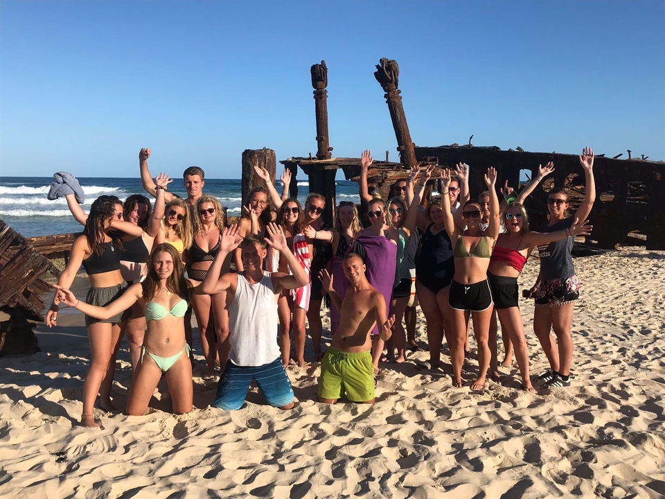 Groupe de personnes posant sur une plage près d'une épave de navire