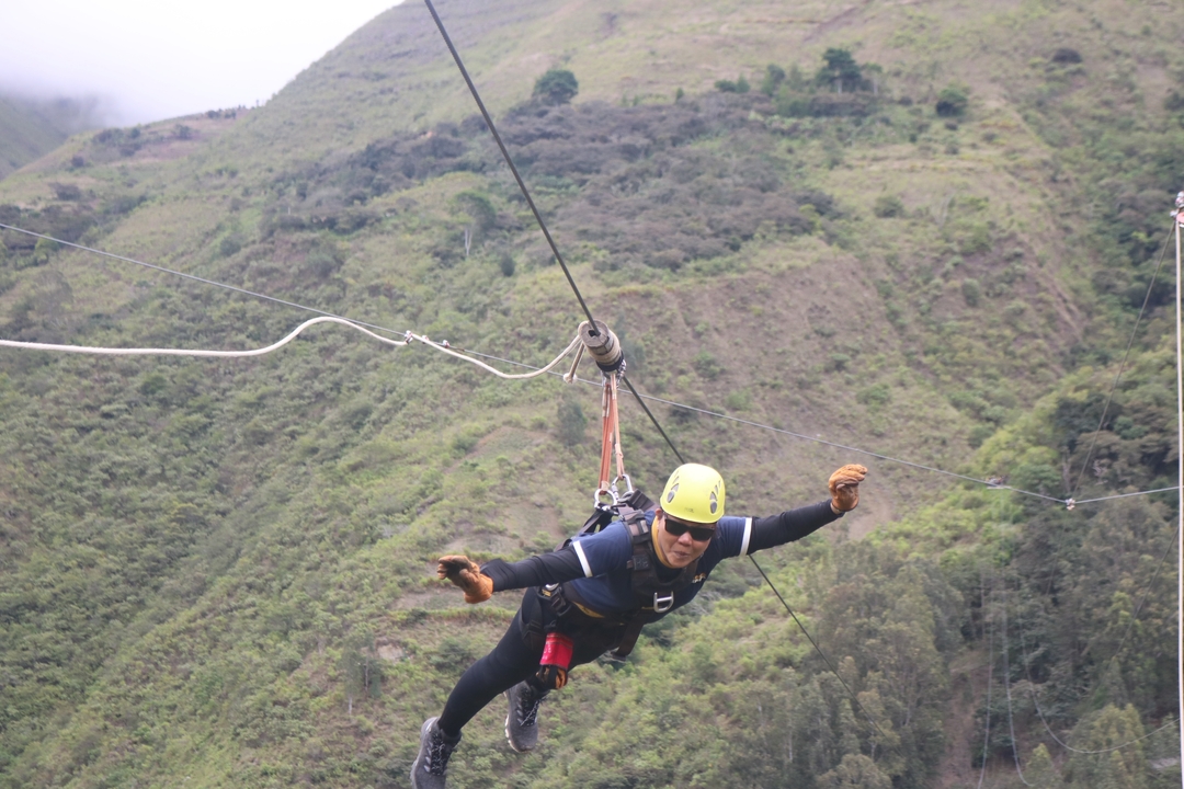 Personne faisant de la tyrolienne au-dessus d'un paysage verdoyant.