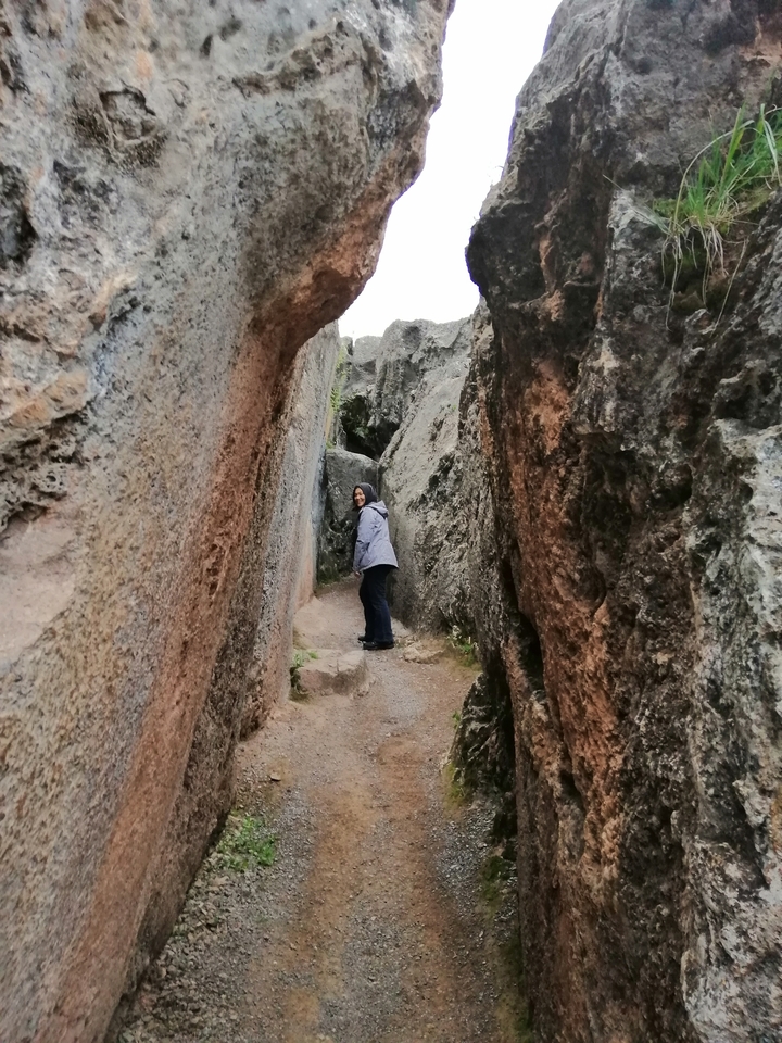 Personne debout entre des formations rocheuses sur un sentier étroit.