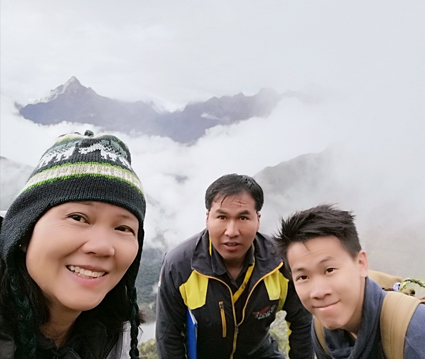Trois personnes souriantes avec un paysage brumeux et montagneux en arrière-plan.