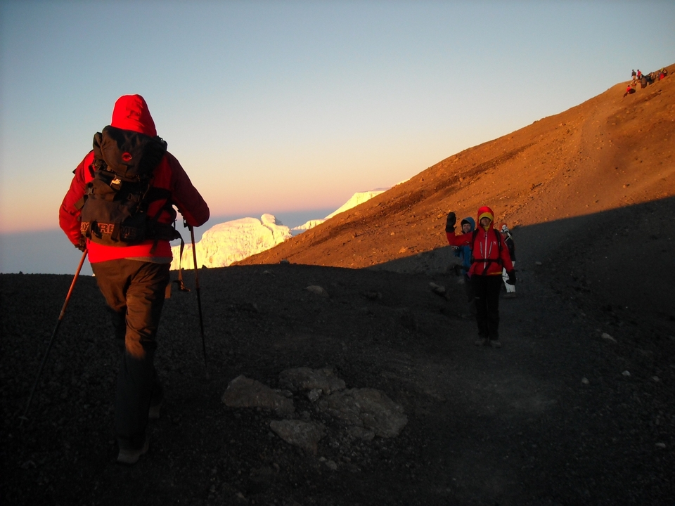 Randonneurs escaladant une montagne au lever du soleil, pic enneigé au loin.