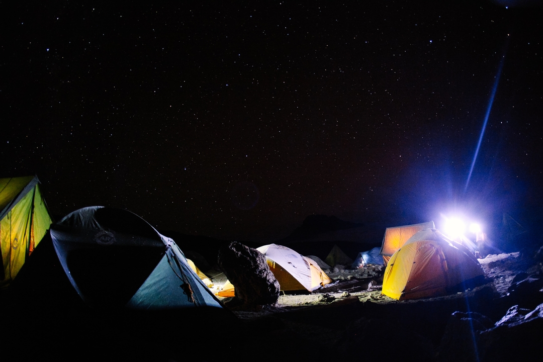 Terrain de camping avec des tentes sous un ciel étoilé la nuit.
