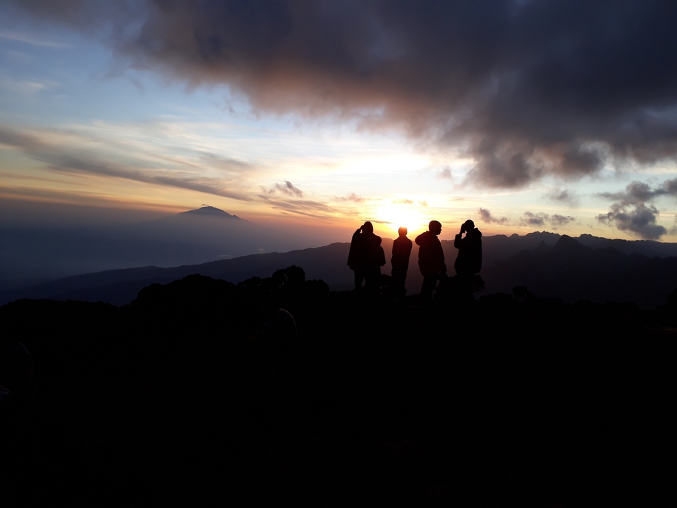 Des silhouettes de personnes regardant un coucher de soleil sur un paysage montagneux.