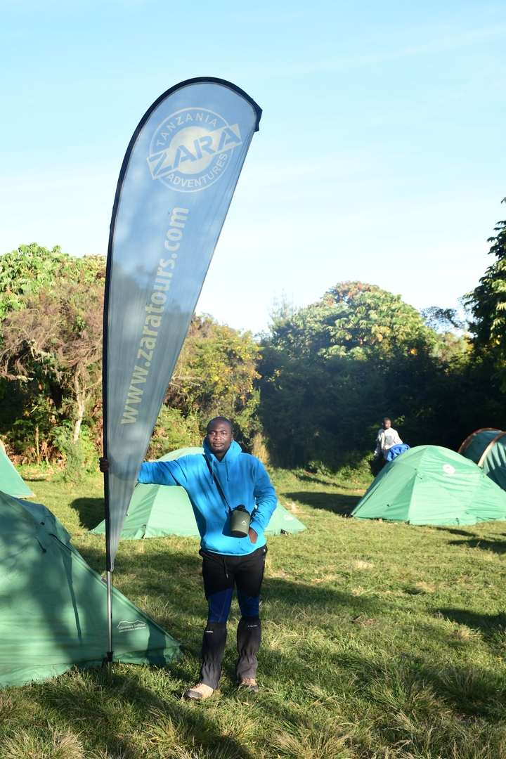 Personne tenant un drapeau d'entreprise à côté de tentes vertes dans un camping.