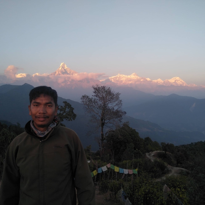 Trekker poses before snow-capped Himalayan peaks glowing pink in the early morning light.