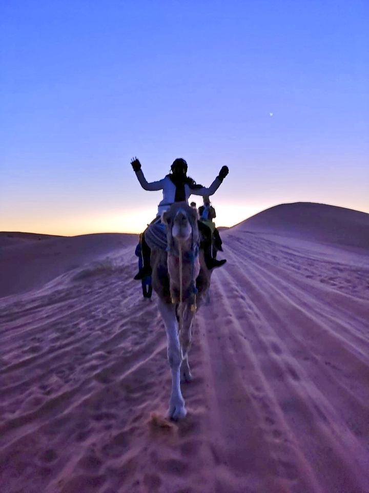 Personne montant un chameau sur des dunes de sable au coucher du soleil.