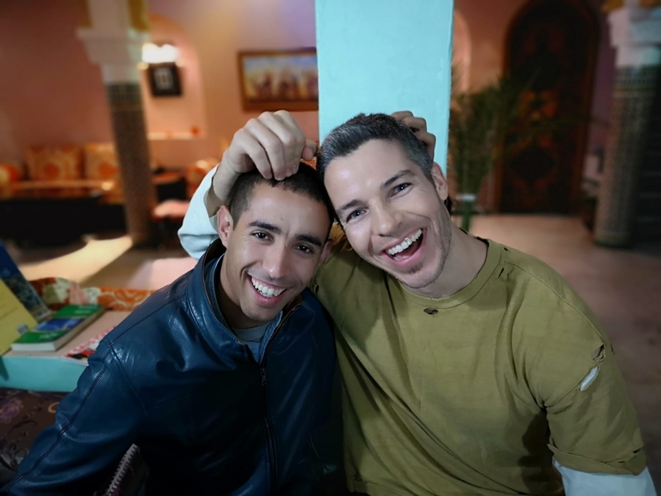Deux hommes souriants assis ensemble à l'intérieur.