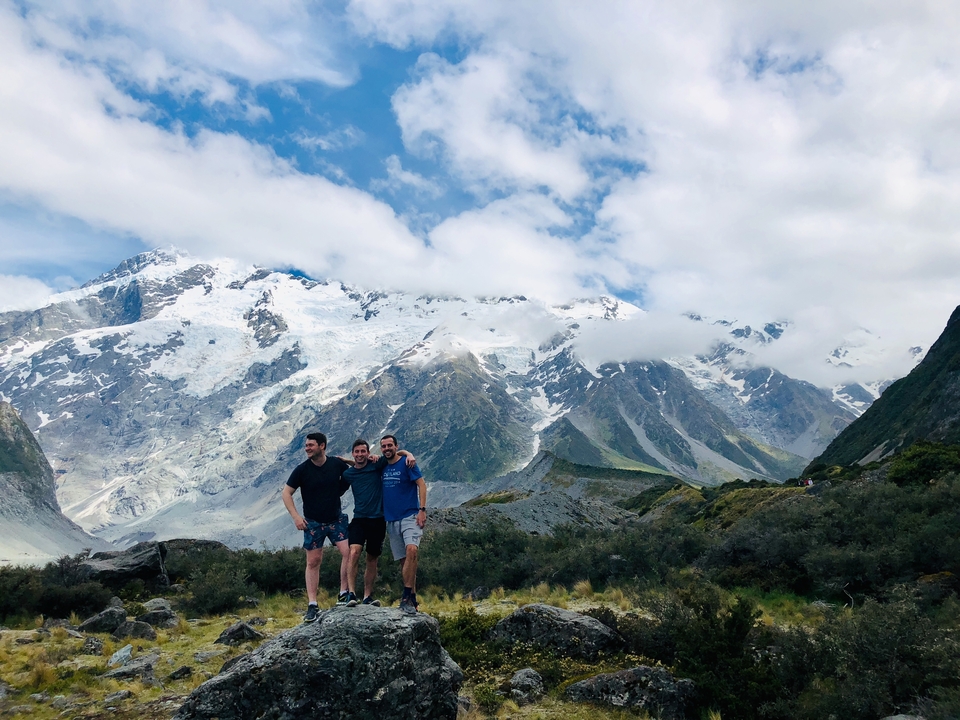 Groupe de trois hommes posant devant des montagnes enneigées.