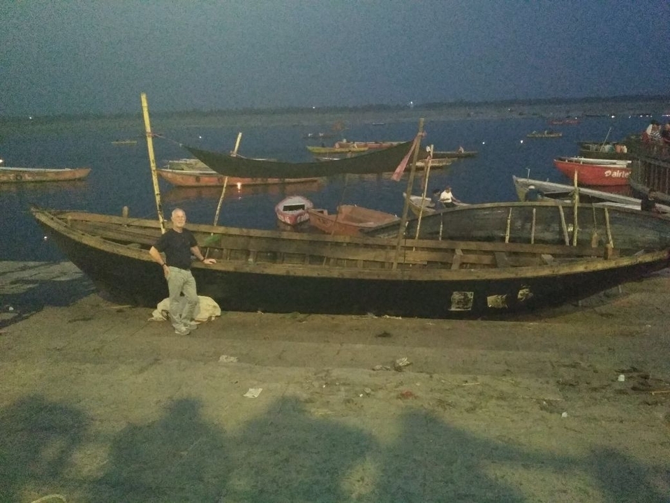 Grainy night photo of a man posing beside a wooden boat on a dark riverbank.