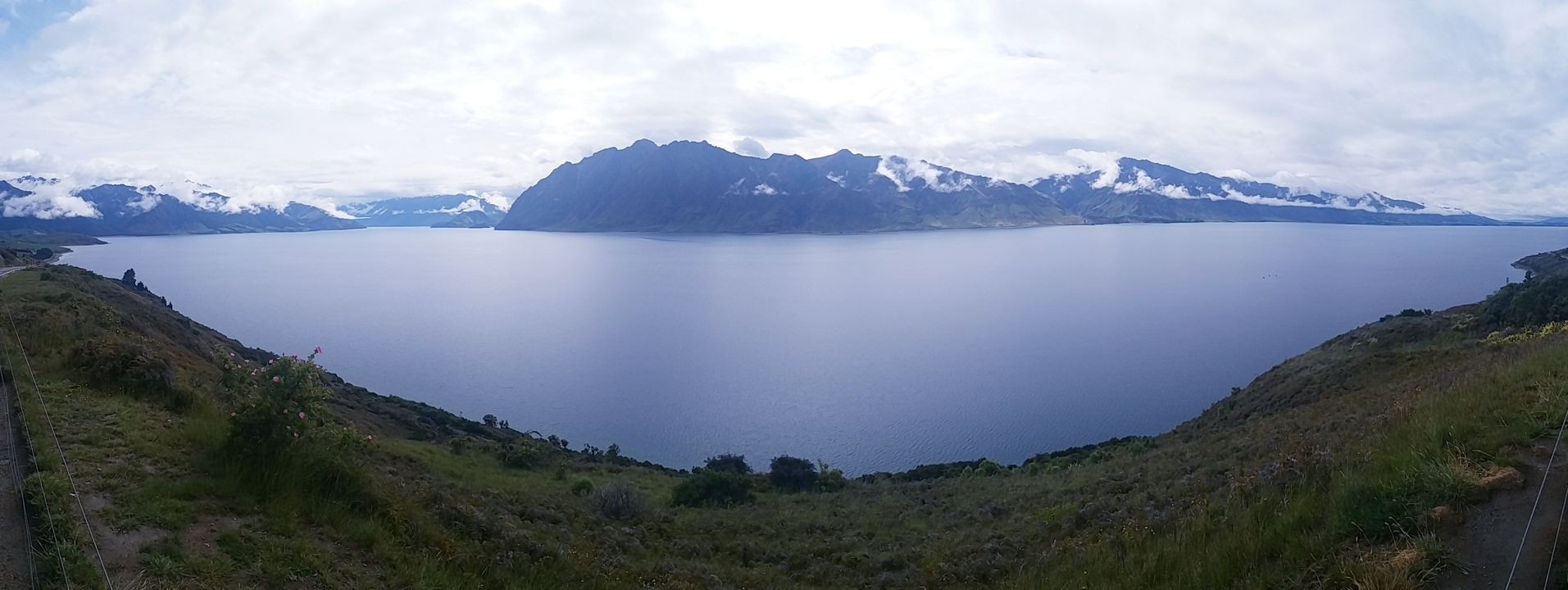 Grande étendue d'eau entourée de montagnes sous un ciel nuageux.