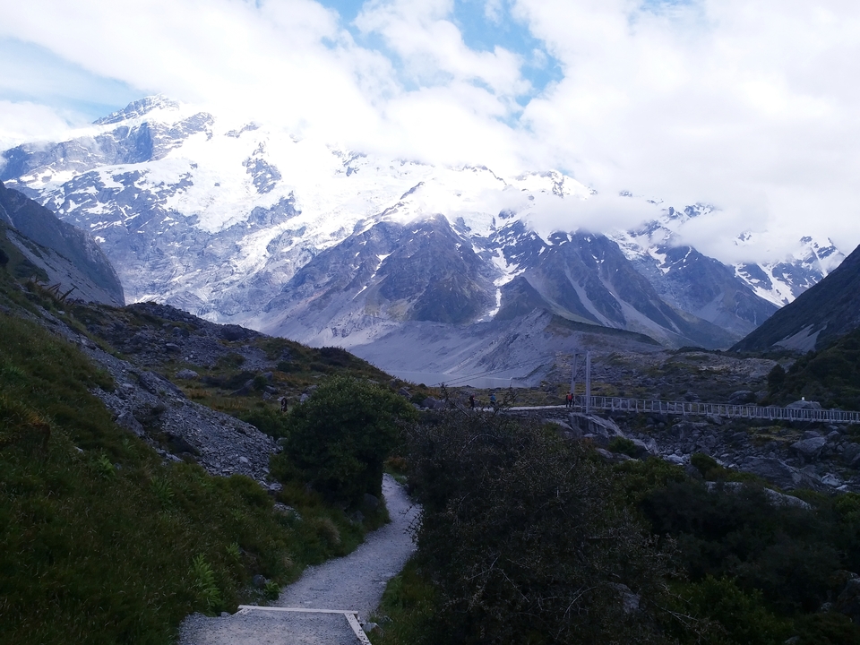 Montagnes enneigées avec un pont menant vers un sentier lointain.