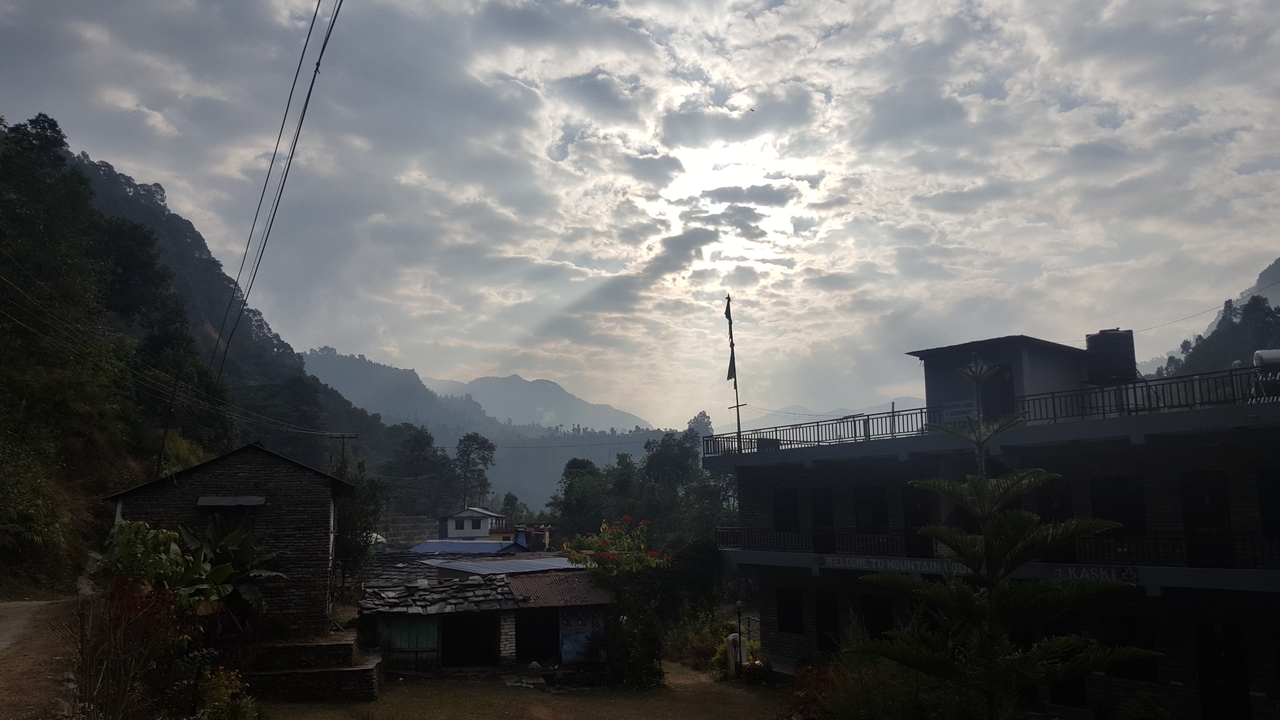 Bâtiments de village avec un ciel nuageux et des collines lointaines.