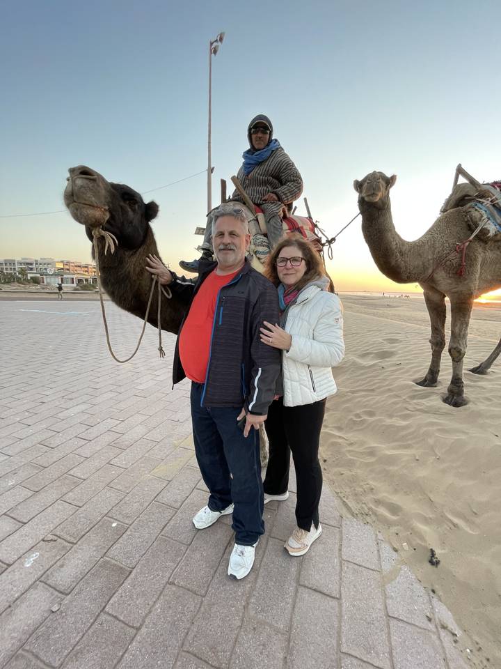 Deux personnes devant des chameaux sur une plage au crépuscule.
