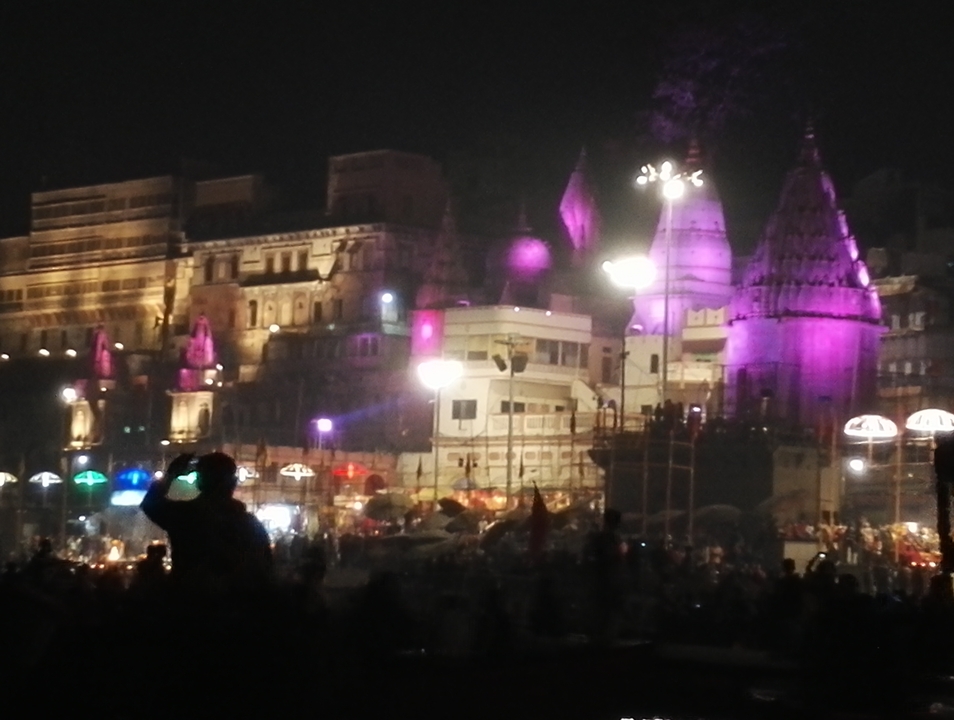 Vue nocturne d'un bâtiment illuminé de couleurs avec des gens et de petits groupes.