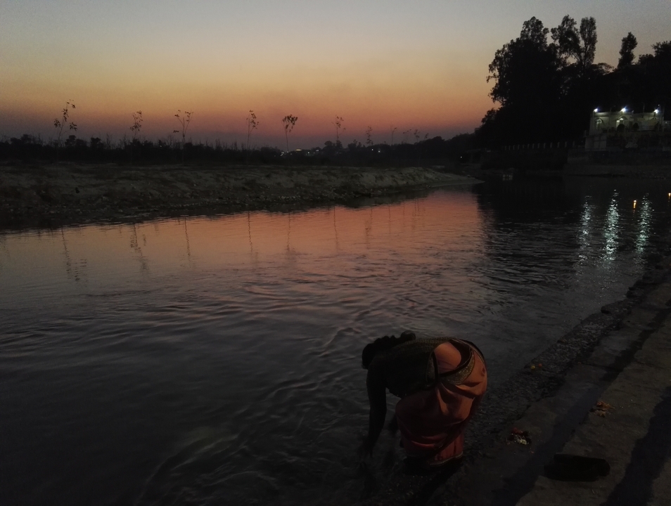 Silhouette d'une personne au bord de la rivière au coucher du soleil.