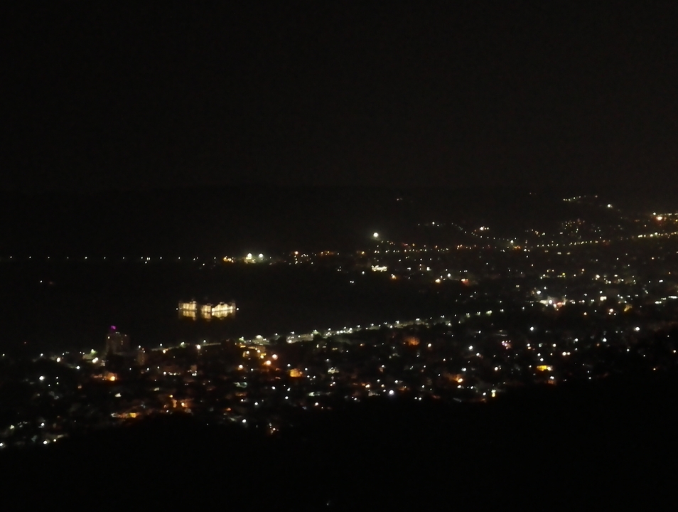 Paysage nocturne urbain montrant des lumières lointaines et un plan d'eau.