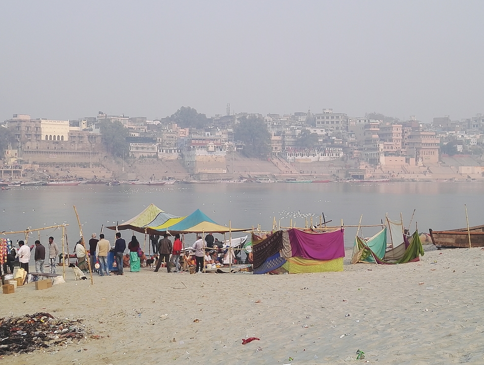 Des tentes and des personnes près d'une rivière avec des bâtiments en arrière-plan.