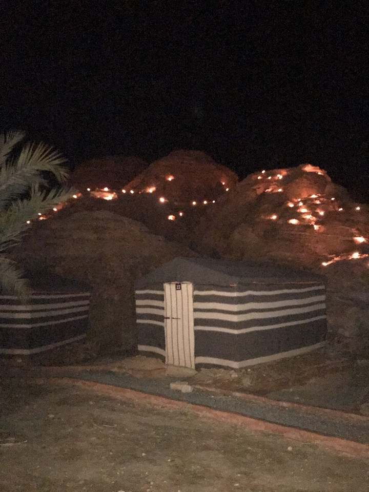 Scène nocturne avec des tentes et des montagnes illuminées par de petites lumières.