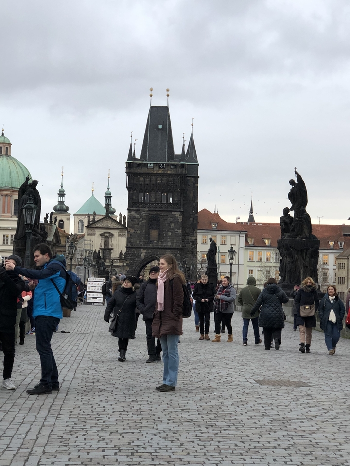 Touristes marchant sur le pont Charles avec des statues visibles.