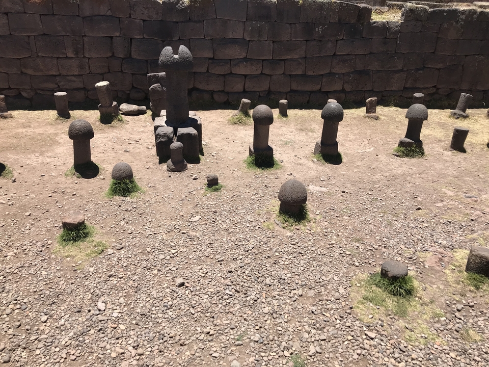 Stone formations in a circular arrangement on a dirt ground with a stone wall in the background.