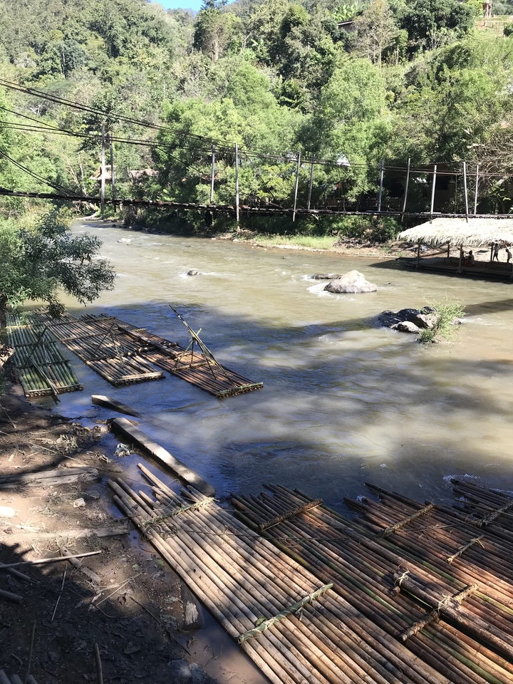 Radeaux de bambou sur une rivière avec un pont en arrière-plan.