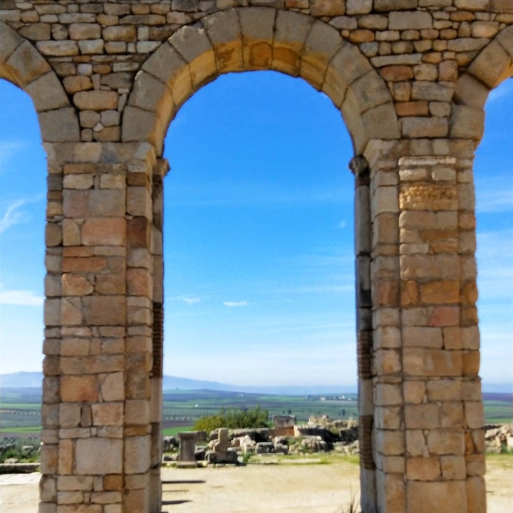 Blurred image of a stone arch against a blue sky.