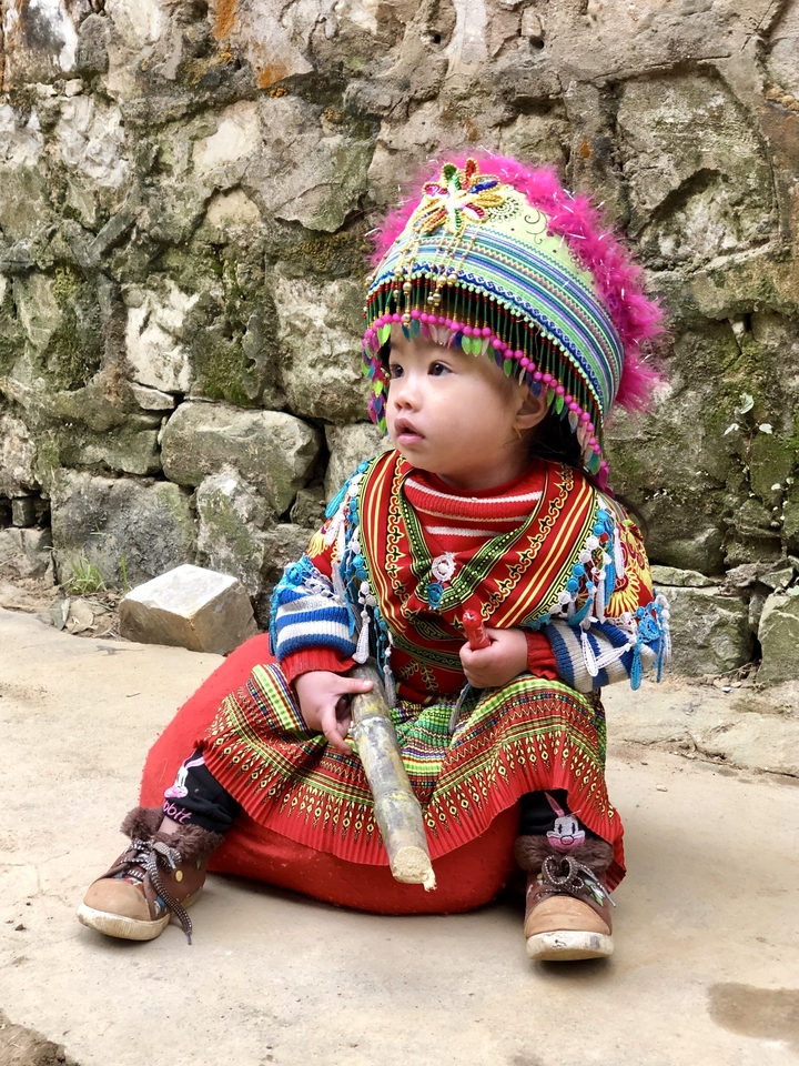 Enfant en tenue traditionnelle colorée dans un cadre naturel.