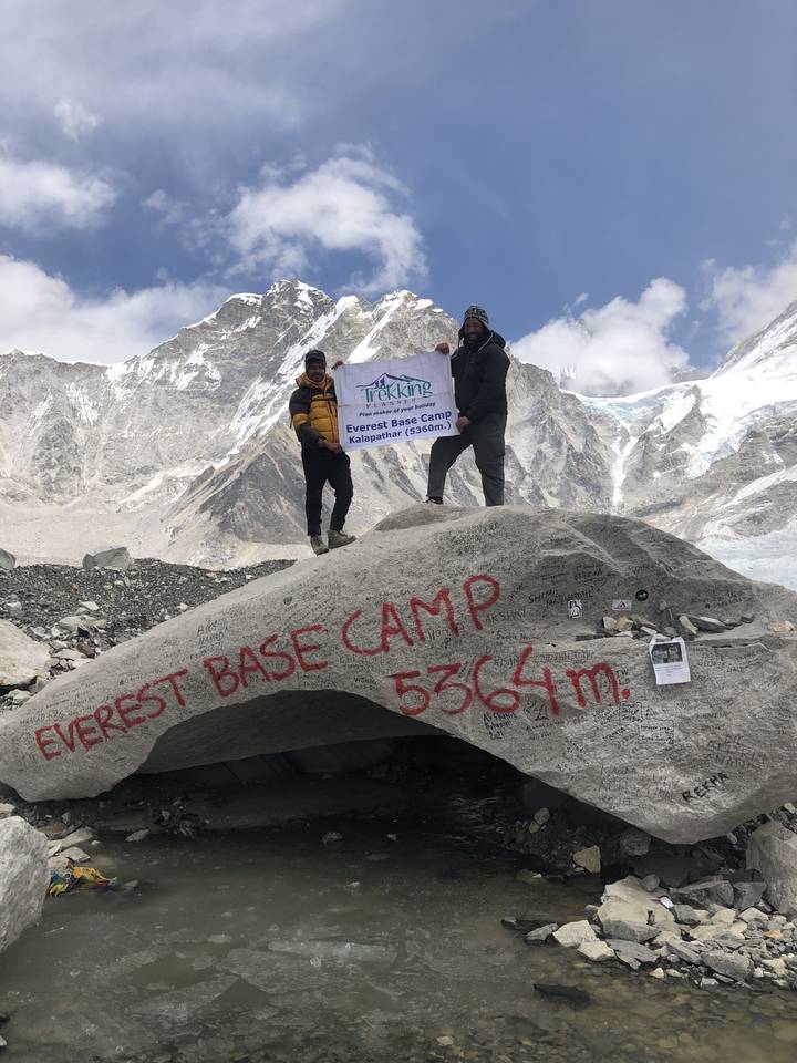Deux personnes debout sur un gros rocher avec un panneau du camp de base de l'Everest.