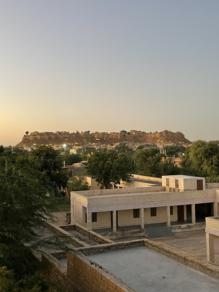 Vue du fort de Jaisalmer au crépuscule, entouré d'arbres et de bâtiments.