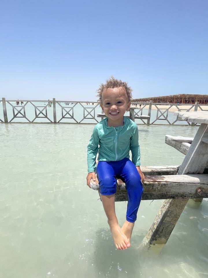 Niño sentado en un muelle cerca de un cuerpo de agua.
