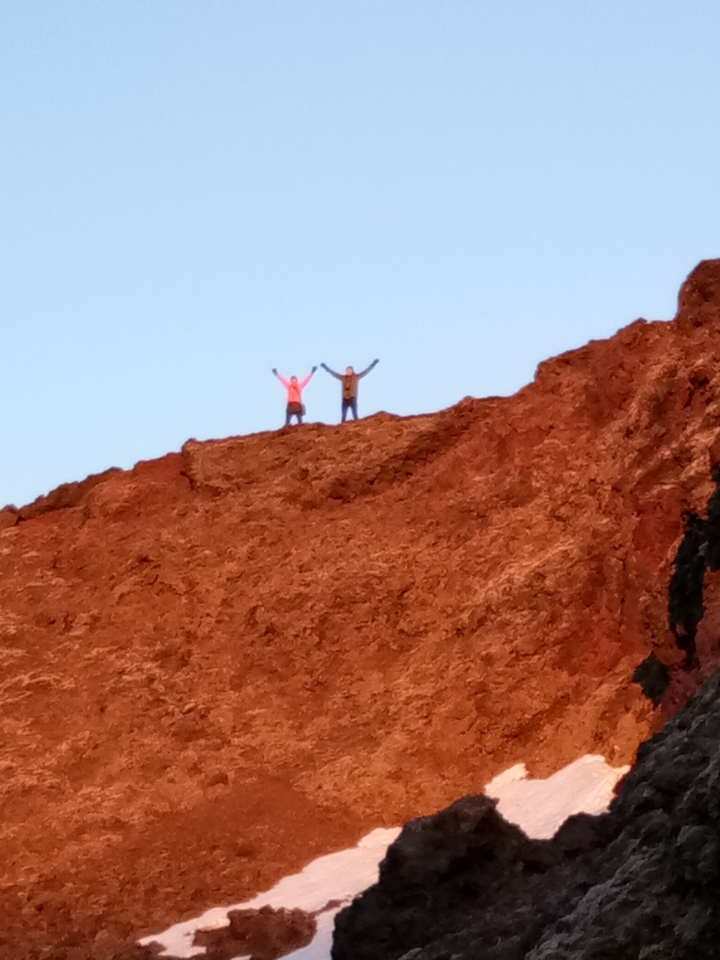 Deux personnes au sommet d'une falaise rocheuse, qui acclament.