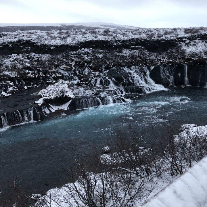 Waterfall flowing over rocks into a river.