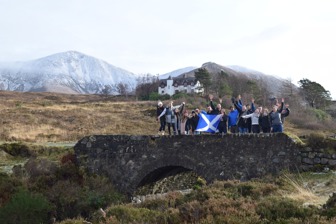Un groupe de personnes tenant un drapeau écossais sur un pont de pierre avec des montagnes.