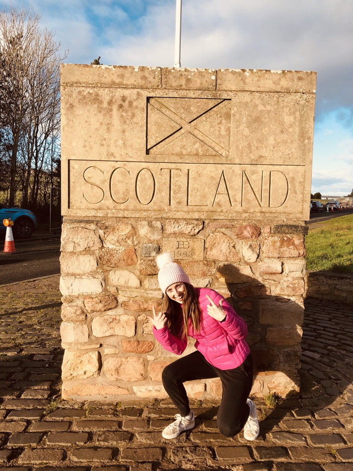 Une personne posant à côté d'un panneau en pierre marquant la frontière écossaise.