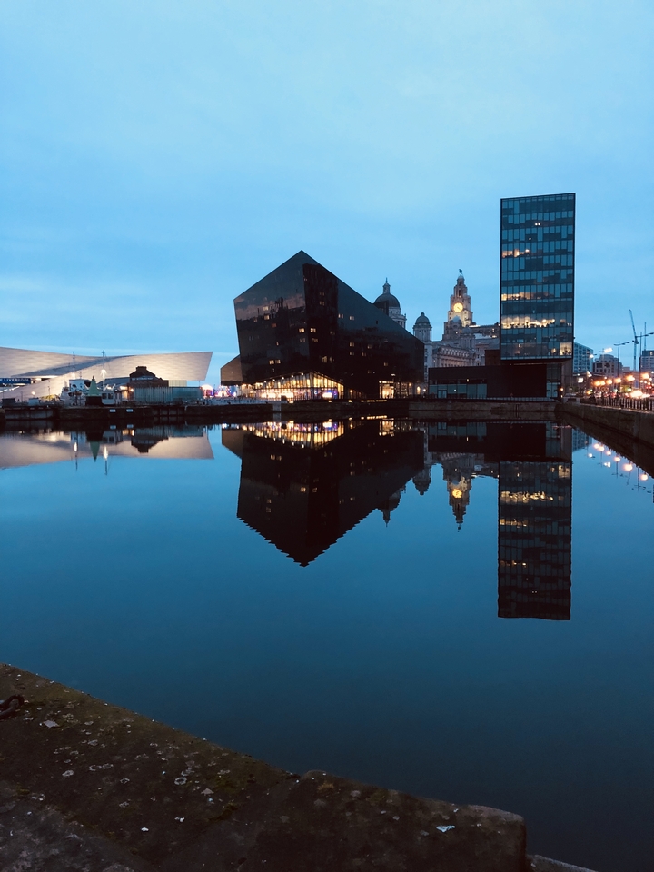 Bâtiments modernes se reflétant sur un plan d'eau dans un environnement urbain.