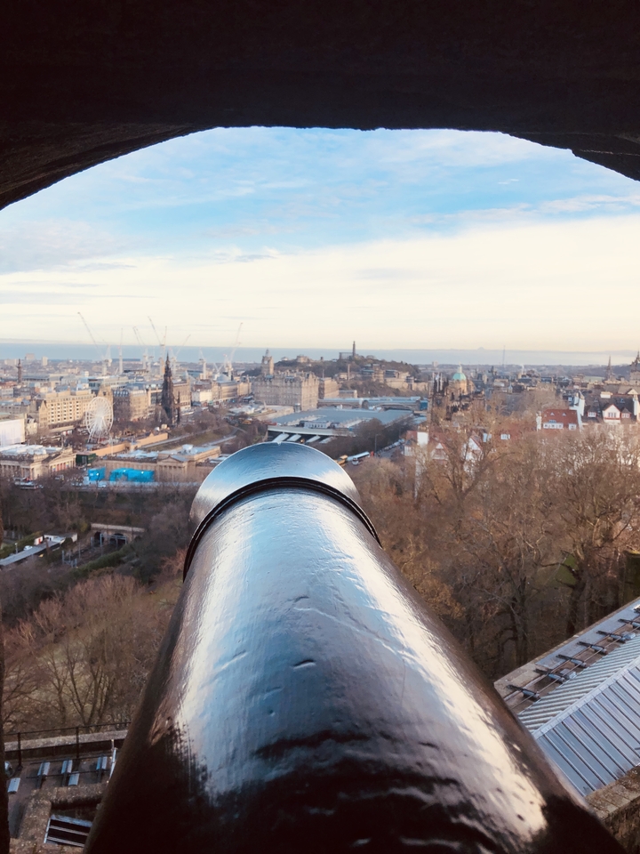 Overlooking a cityscape with a large cannon in the foreground.
**French translation:**
Surplombant un paysage urbain avec un grand canon au premier plan.
