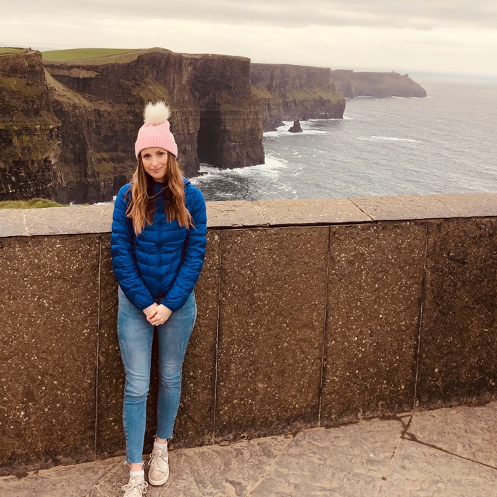 Une personne debout sur une falaise avec la mer en arrière-plan.