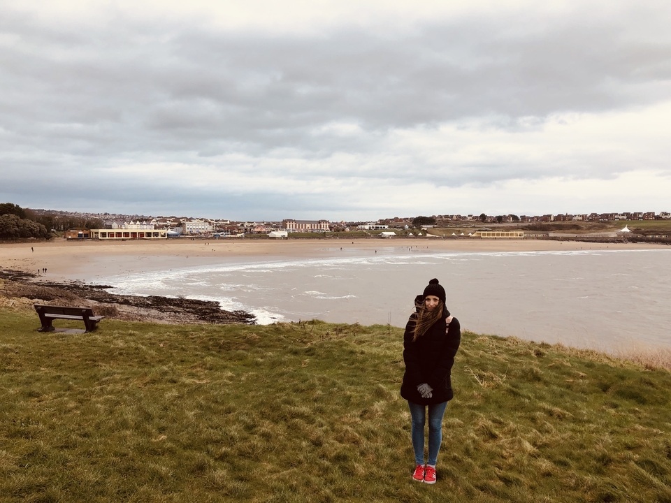 Une personne debout sur une colline herbeuse surplombant une ville côtière.