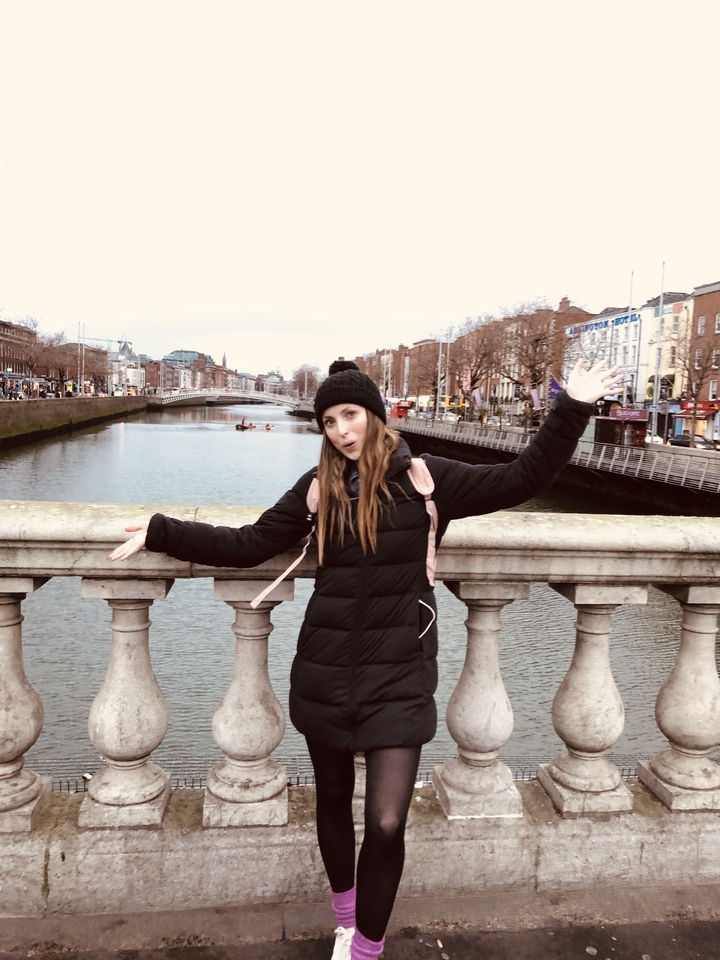 Une personne qui pose sur un pont avec une rivière et des bâtiments de la ville.